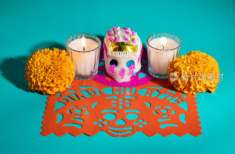 死糖骷髅日(calavera)的祭奠蜡烛和金盏花的campasuchil花橙papel picado在蓝绿色背景，Dia de Muertos的概念